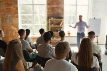 Männlicher Redner hält Vortrag im Saal der Universitätswerkstatt. Audienz- oder Konferenzsaal. Rückansicht unerkannter Teilnehmer im Publikum. Wissenschaftliche Konferenzveranstaltung, Schulung. Bildungskonzept.